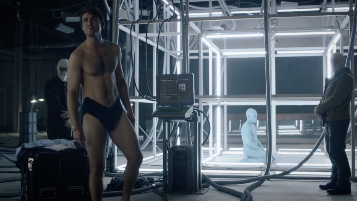 Joe Keene in his underwear standing in front of a caged Dr. Manhattan