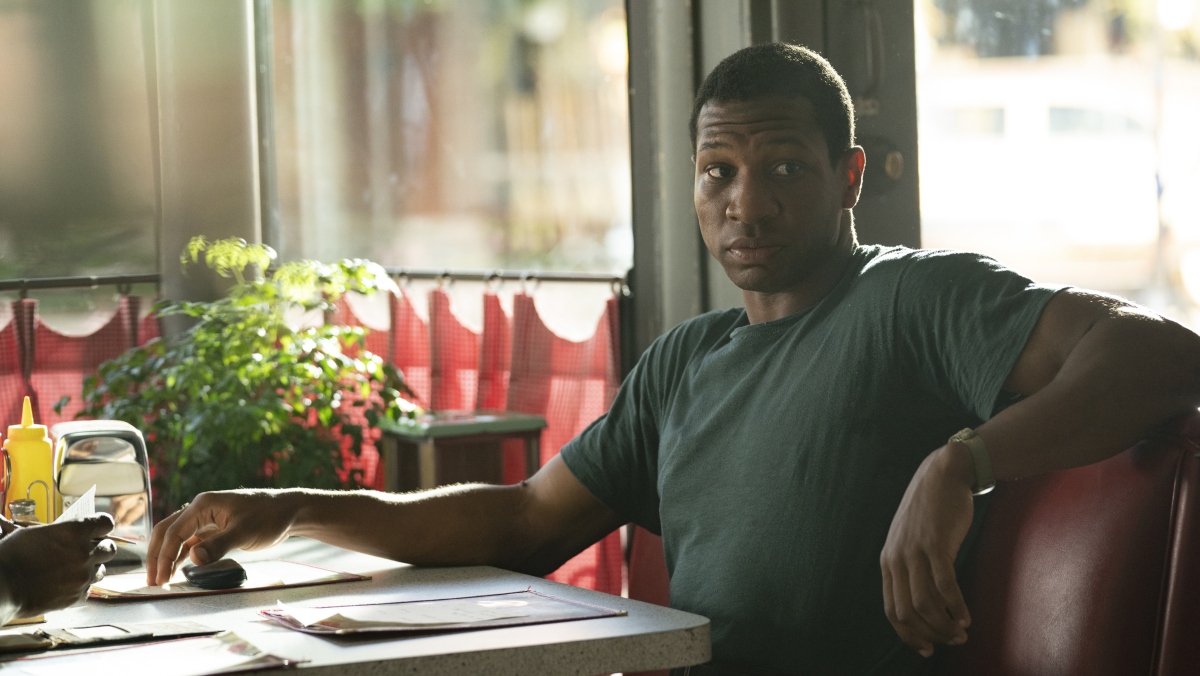 A Black man in a green shirt sits in a red diner booth