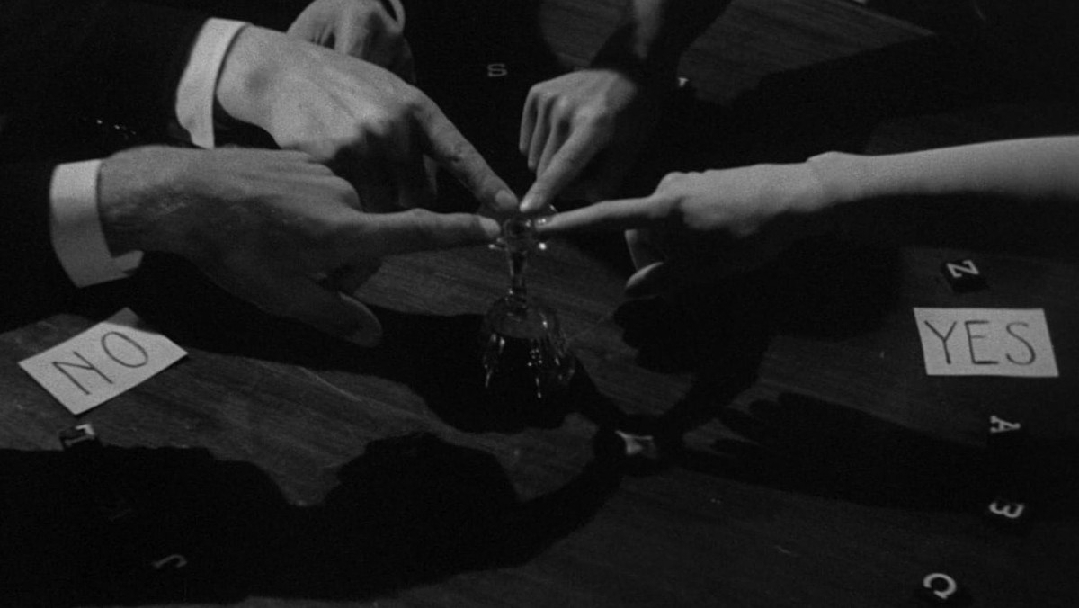 Hands move a makeshift Ouija board in a still from The Uninvited.