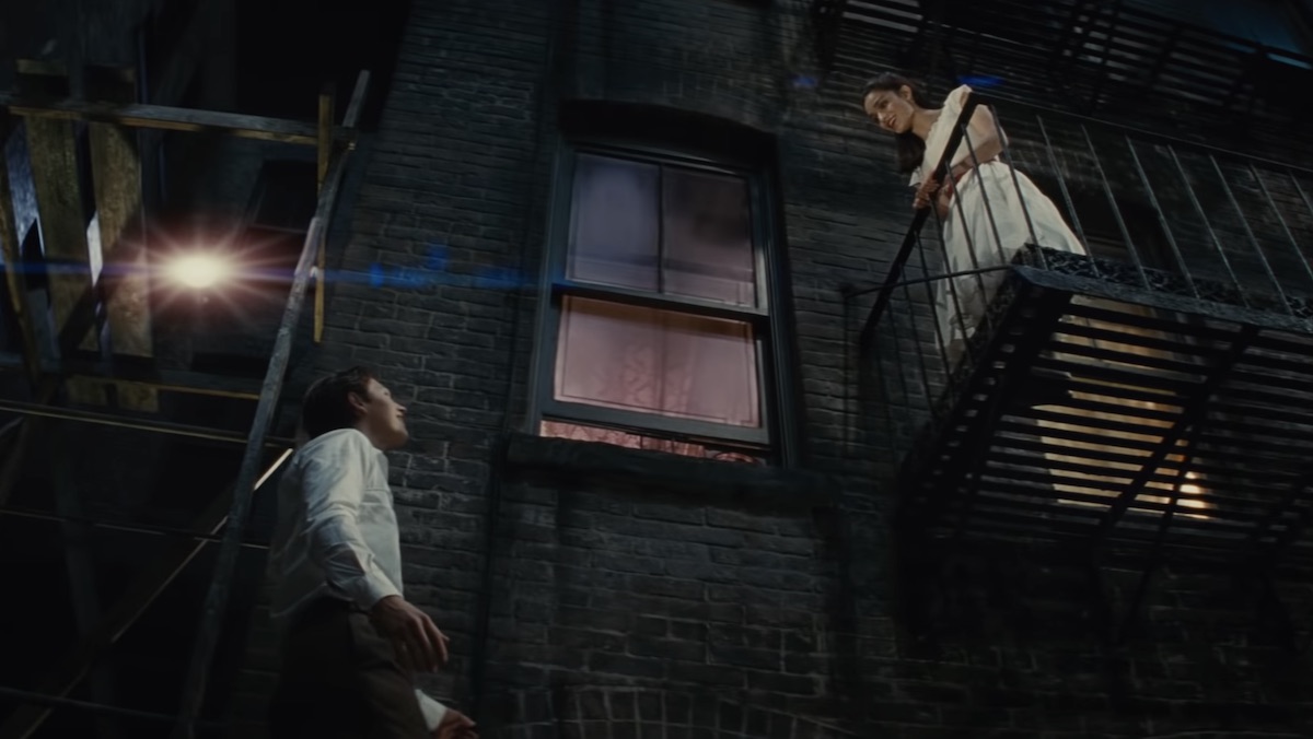 Ansel Elgort's Tony looks up at Rachel Zegler's María standing on a fire escape in Steven Spielberg's West Side Story