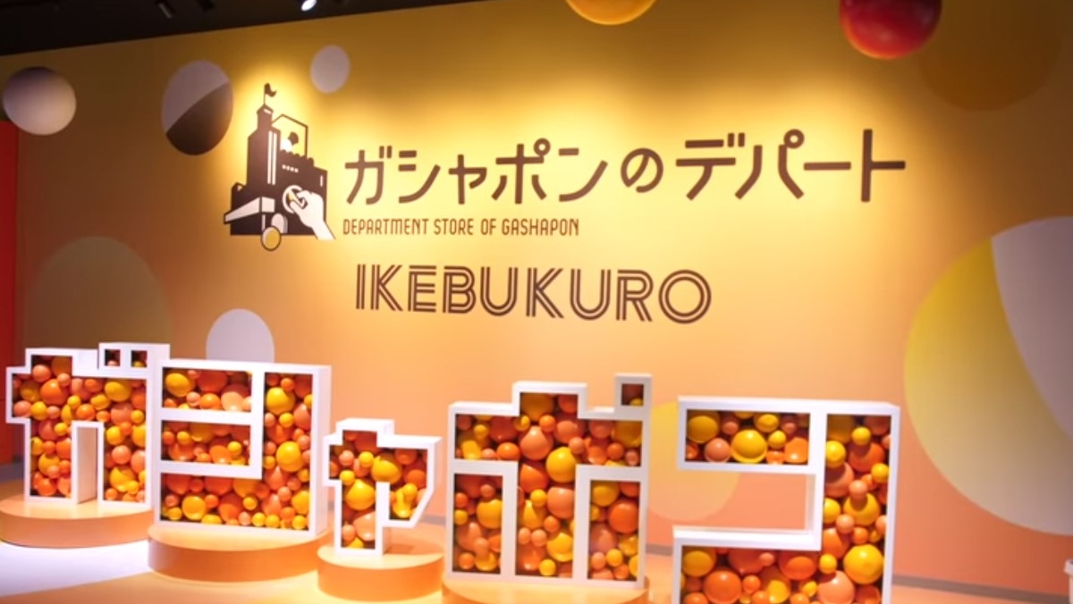 a photo of orange and yellow plastic balls inside white geometric shapes with the word Ikebukuro and Gashapon department store written in japanese. 