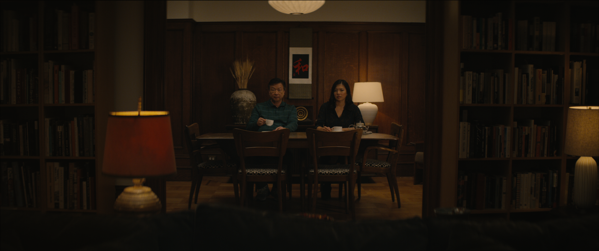 a man and woman sit at a dining room table in a darkened room with one white lamp