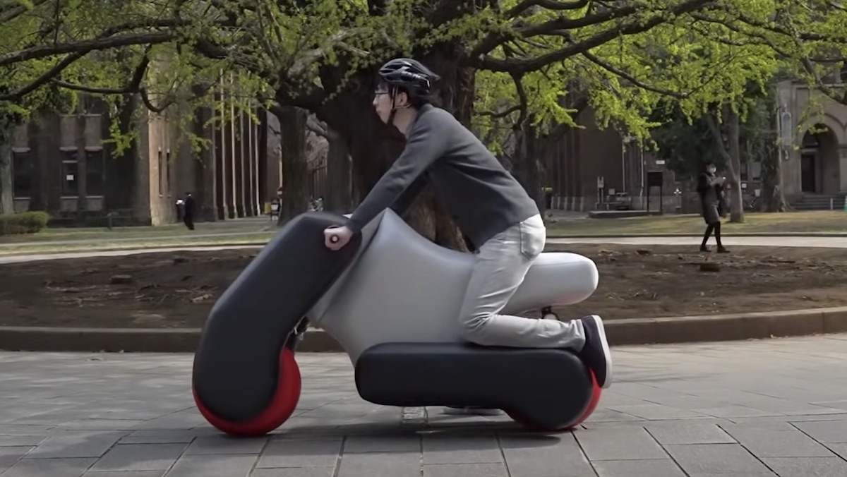 A man with a bike helmet sits on an inflatable motorcycle in a park