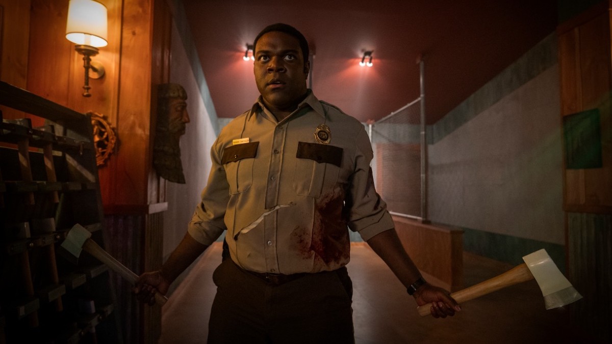 Sam Richardson, dressed as a park ranger, wields a hatchet and a large axe.