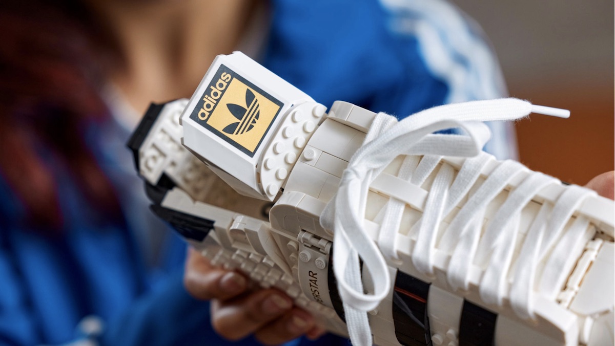 A woman holds A white and black LEGo replica of an adidas sneaker