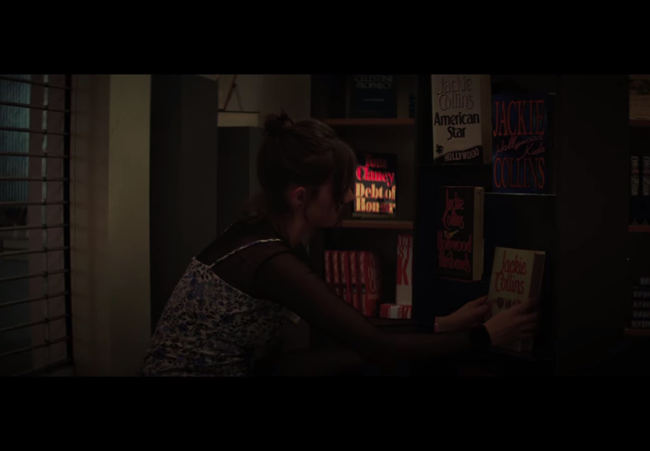 a girl puts Jackie Collins novels on a bookshelf 