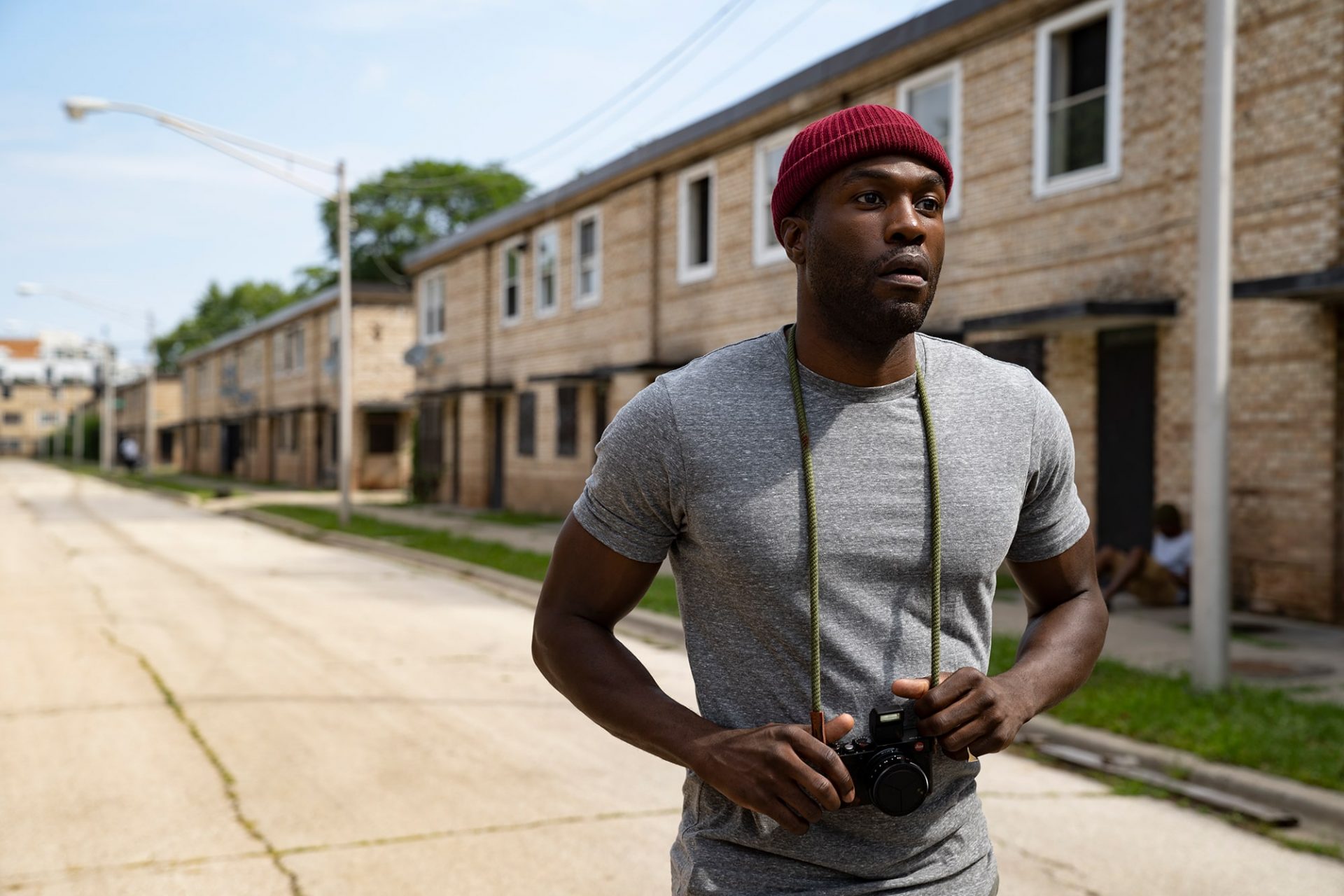 A man wearing a red knit cap stands in a street with a camera in Candyman film