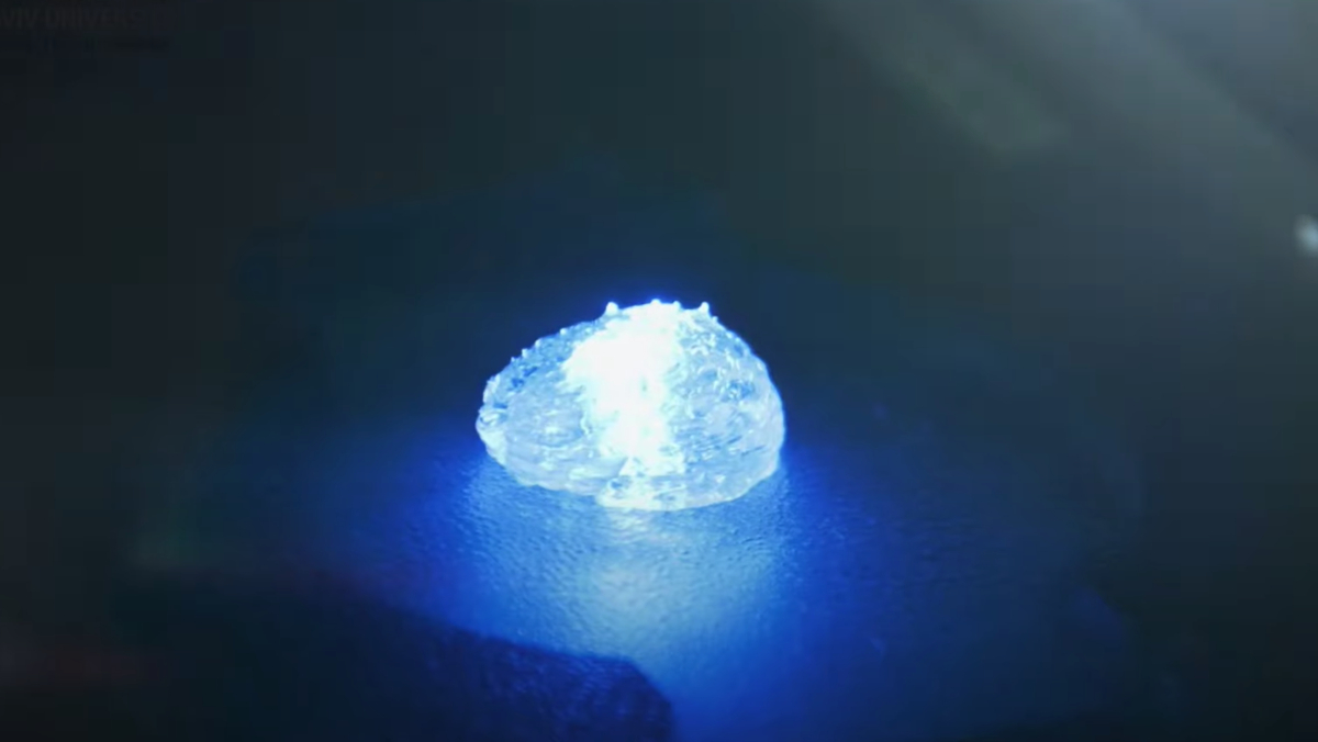 A glowing, blue 3D-printed hunk of tumor sitting on a dark surface in a lab.