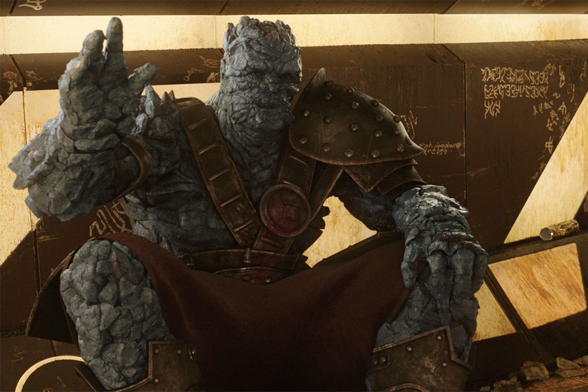 In a still from Thor: Ragnarok the rock alien Korg sits in front of a lit up wall