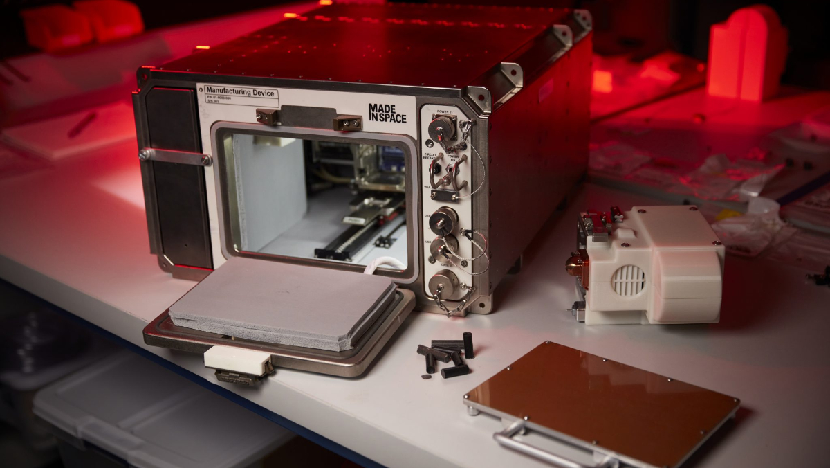 A 3D printer the size of a microwave with its door open, underneath dark-red lights.