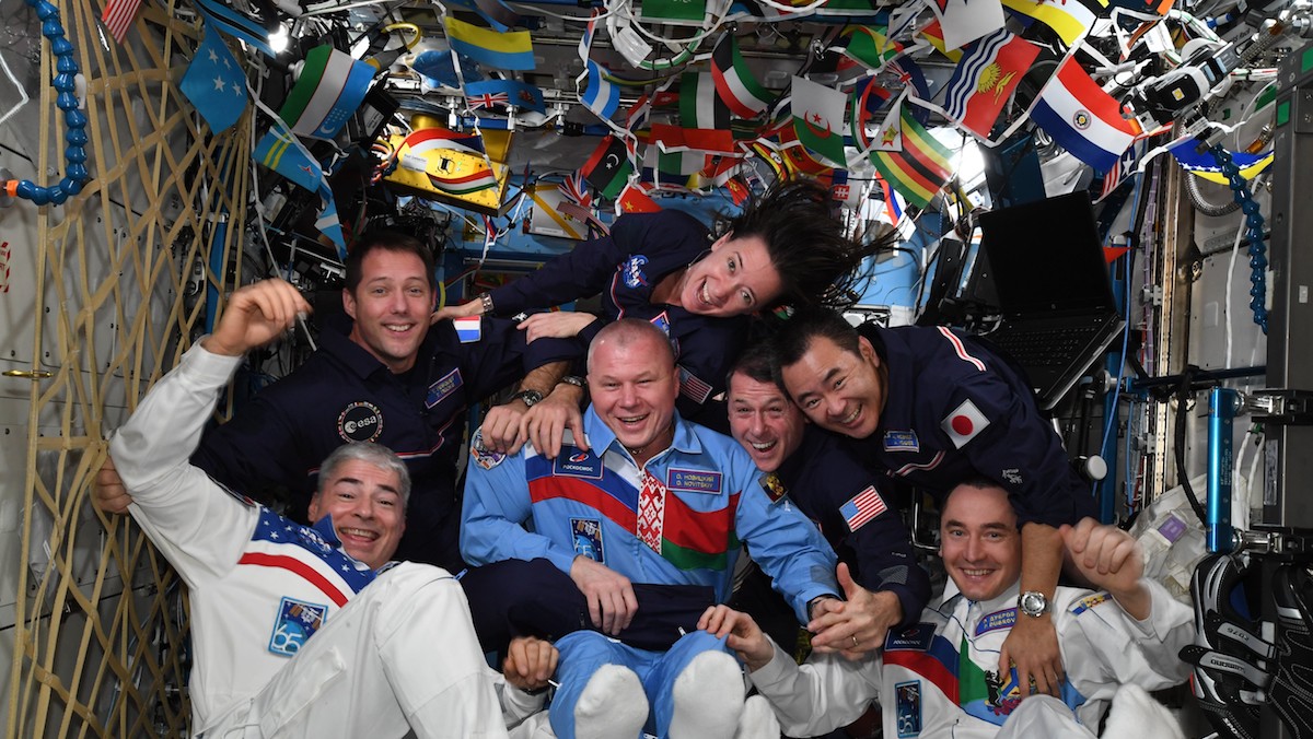 astronauts in space pose with flags from countries all over Earth