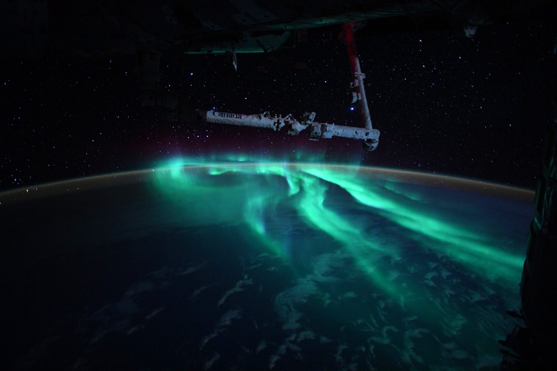 The international space station flying above bluish green auroras over Earth's southern hemisphere.