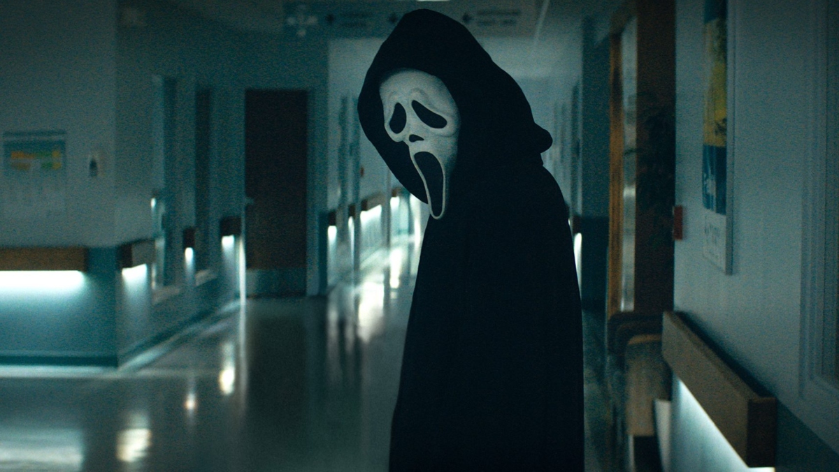 ghostface from scream 2022 stands in a hallway facing the camera