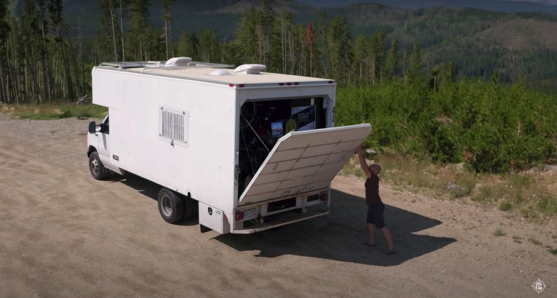 A man shows off the outside of his "stealth studio van," which has a kitchen, bedroom, and office.