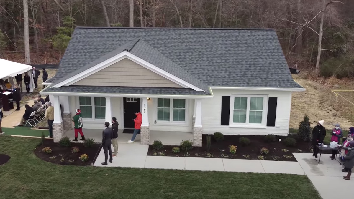 People stand outside a white 3D-printed house from Habitat for Humanity, seen from above