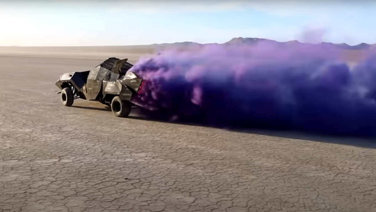 A Batmobile made out of LEGO driving in a desert with purple smoke coming out the back