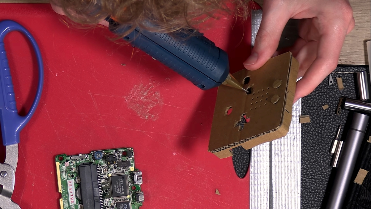 A man's hands using a glue gun to make a Gameboy Advance shell out of cardboard