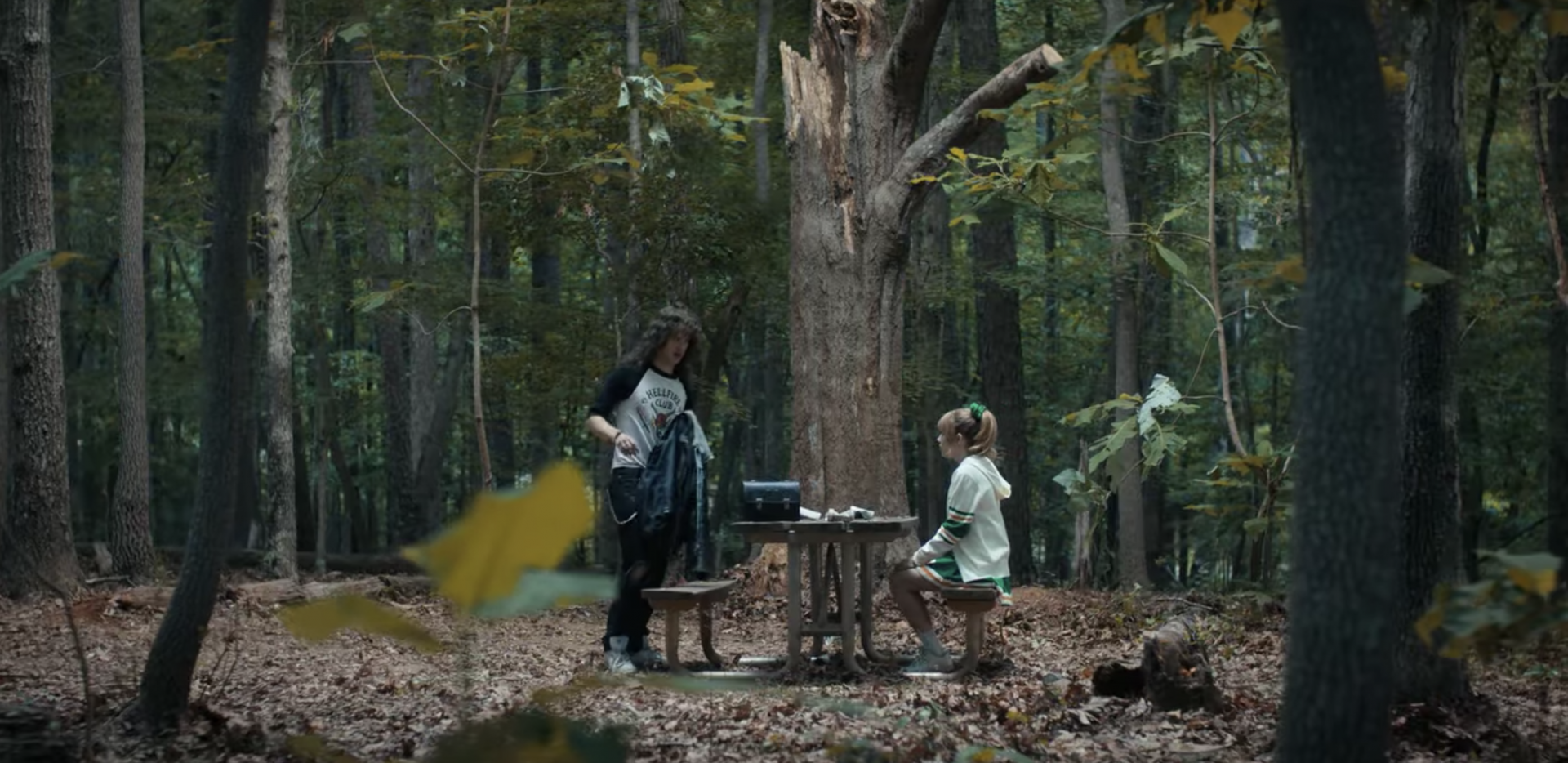 Eddie and Chrissy sitting at a picnic table in the woods in Stranger Things 4