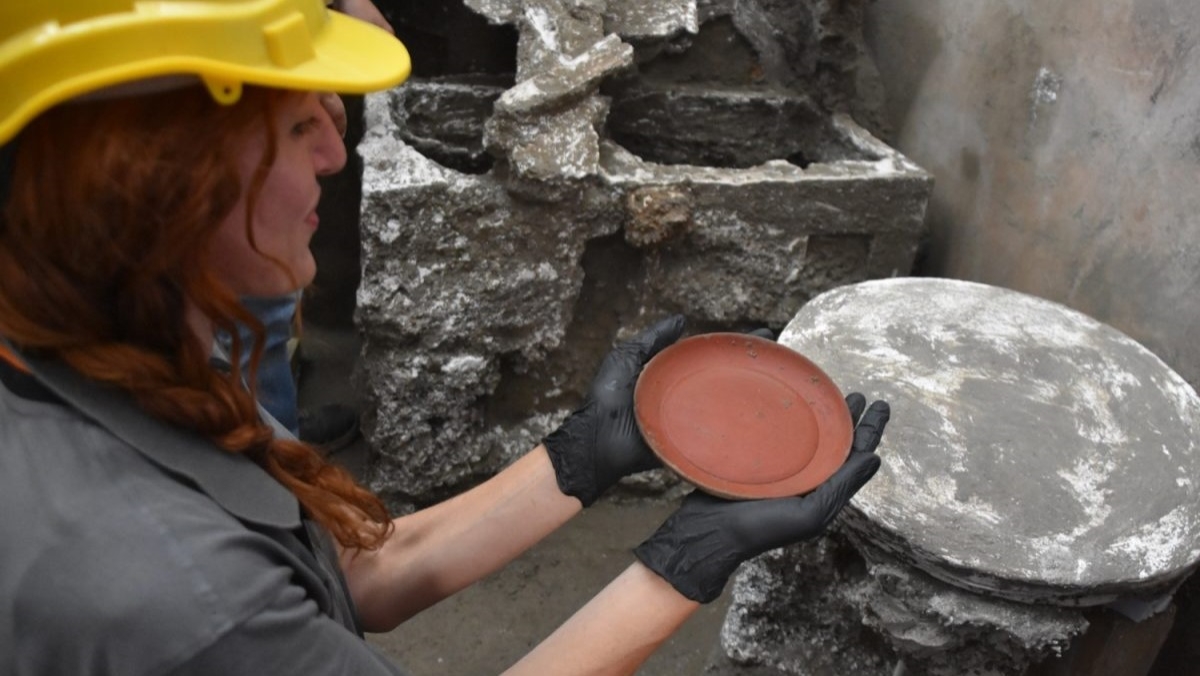 A woman in a hard hat holds a clay plate in her gloved hands