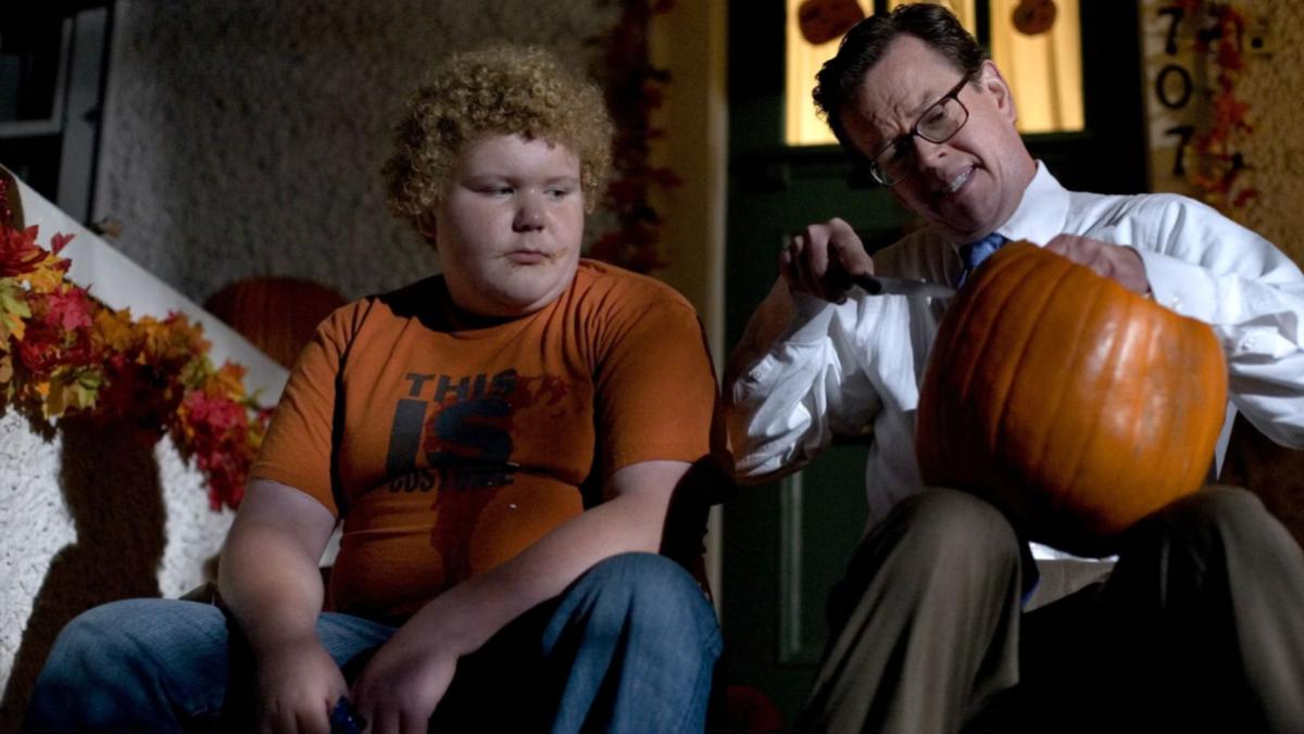 A still from Trick 'R Treat shows an older man played by Dylan Baker carving a pumpkin next to a young boy