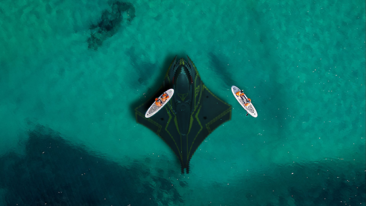 A manta-shaped submarine driving underwater below two paddleboarders