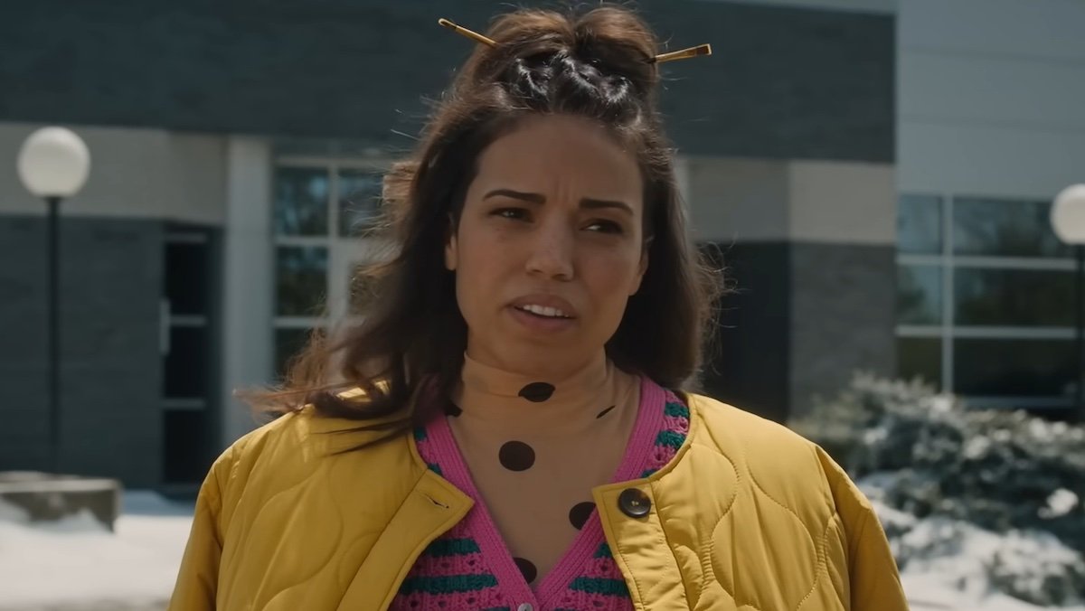 A young Black woman in a yellow coat stands in a parking lot in Paint