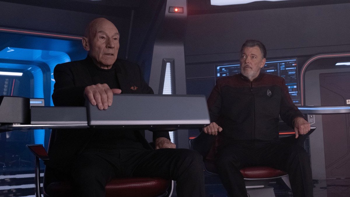 Jean-Luc Picard leans over a console with William Riker beside him on the bridge of the USS Titan in Star Trek: Picard