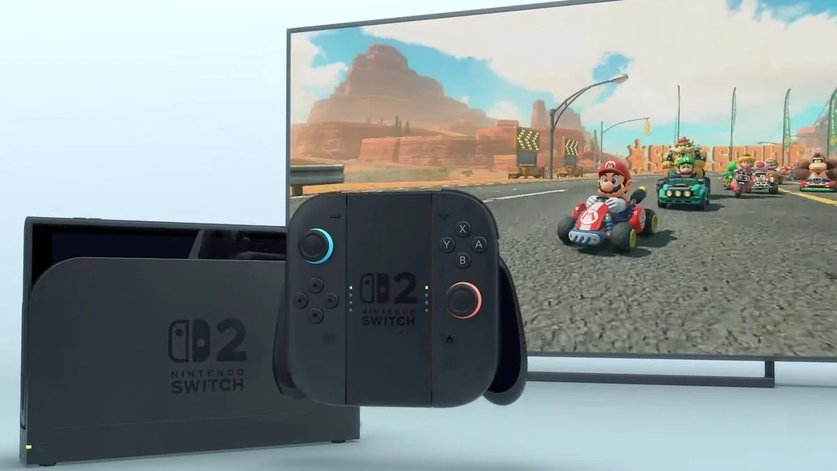 A black Nintendo Switch 2 console in front of a big screen with Mario Kart on it