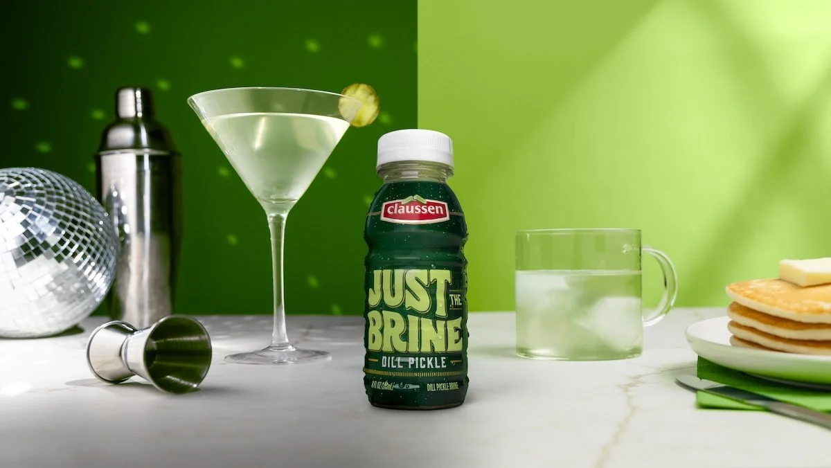 A bottle of Just the Brine with a maritni on one side and a breakfast with a glass on the other