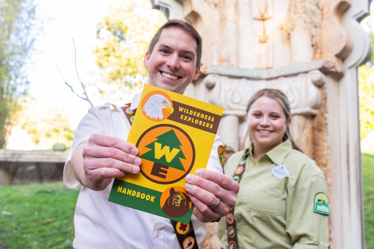 Two cast members holding up a Wildernebss Badge pamphlet for Animal Kingdom