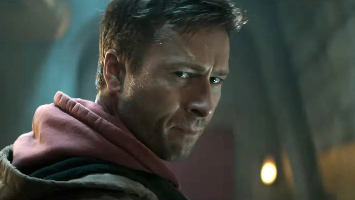 Glen Powell in a hoodie looks back at the camera in The Running Man