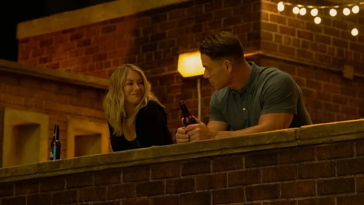 Jennifer Holland as Emilia Harcourt and John Cena as Christopher Smith at a party in Peacemaker season two.
